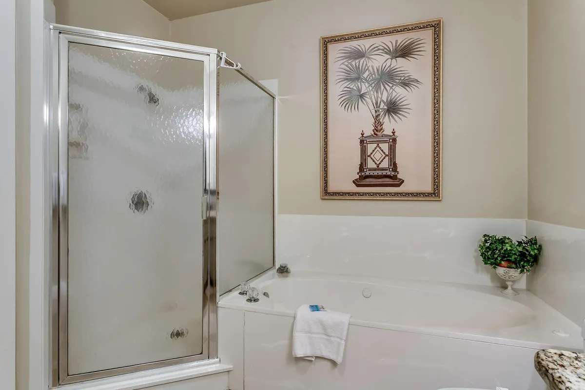 A serene bathroom scene featuring a jacuzzi tub, glass shower enclosure, framed artwork, and a small plant. The space evokes a spa-like atmosphere, ideal for unwinding after a day of exploring the beach or local attractions.