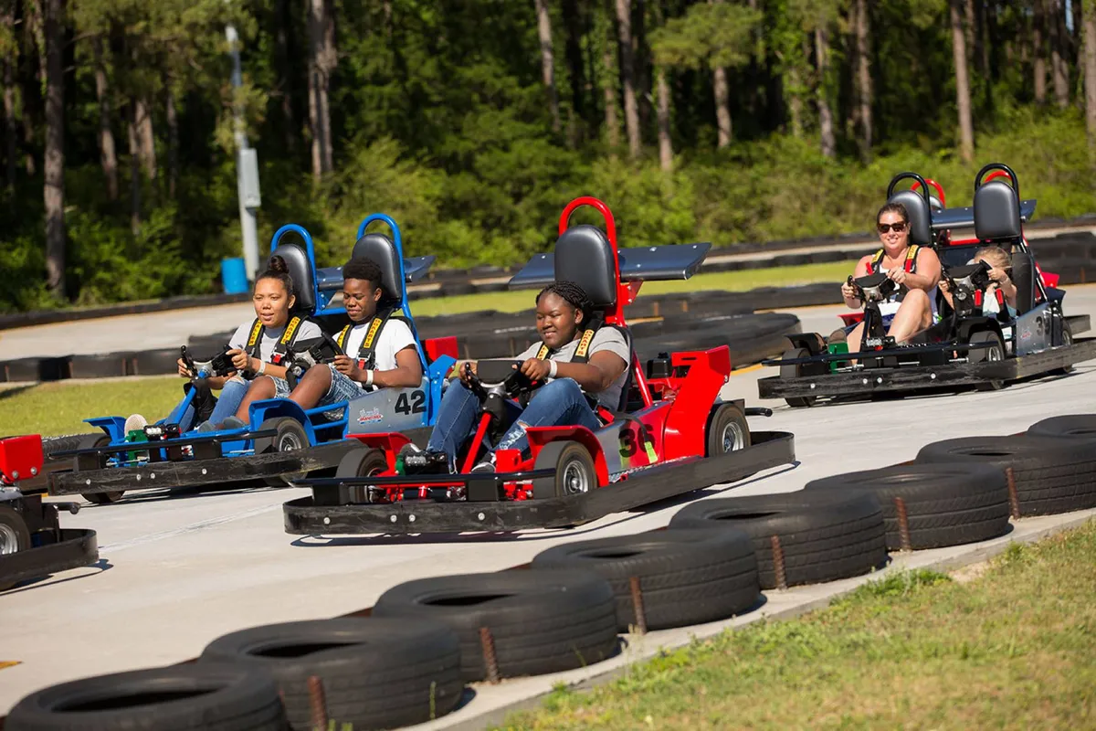 An energetic exterior shot of a go-kart racetrack, with participants navigating tight turns and tire barriers. The focus is on the thrill of competition and shared laughter as families enjoy this playful outdoor attraction.