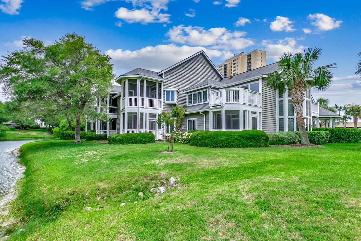The hero image shows the welcoming facade of the Kingston Plantation Windermere condo, framed by lush green landscaping and a tranquil water feature. The scene exudes a calm, inviting atmosphere, with pathways for leisurely strolls, glimpses of balconies perfect for relaxing, and spacious lawns ideal for gatherings or watching local wildlife.