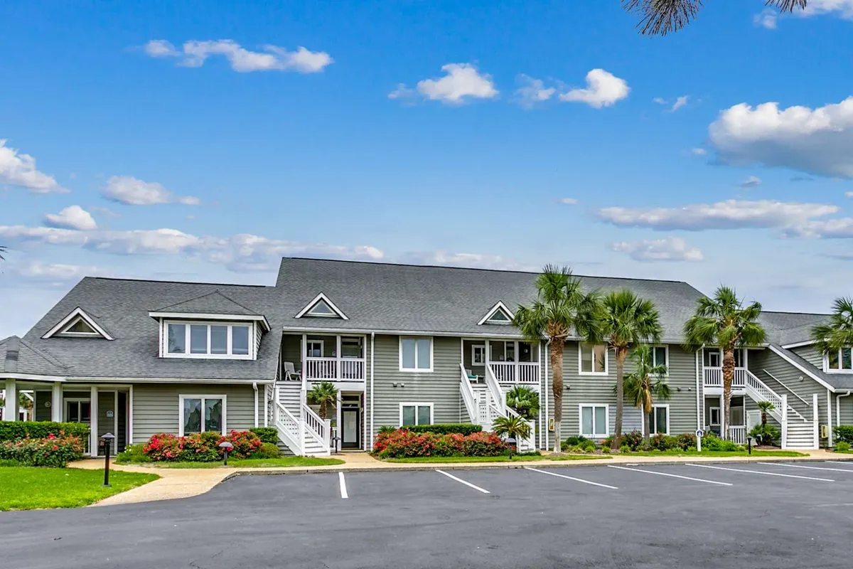 A cheerful exterior view featuring palm trees, colorful flower beds, and balconies with architectural details. Residents are seen relaxing outdoors, socializing on balconies, and strolling in the garden, with the soft light suggesting either morning or evening.