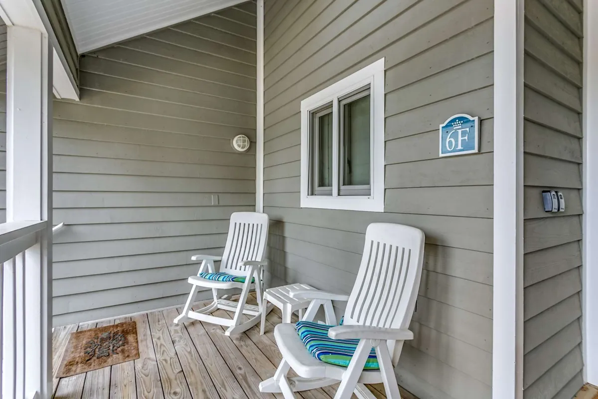 A charming ocean-view front porch with two white rocking chairs, a small side table, and a welcoming mat. The porch radiates relaxation, offering a spot to sip morning coffee, read a book, or enjoy conversations with the sound of the waves in the background.