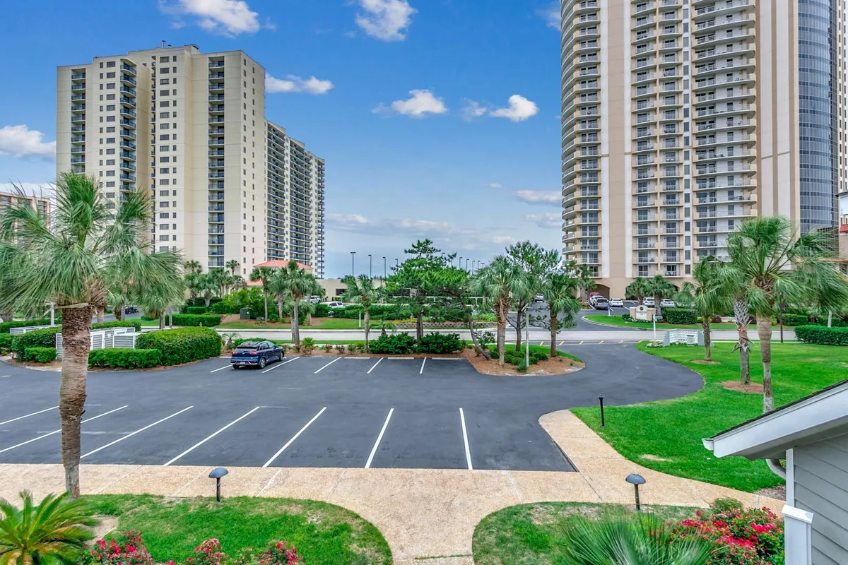 This exterior image showcases the high-rise buildings of a resort community, surrounded by lush green landscaping and palm trees. The scene captures people strolling through manicured gardens, enjoying outdoor gatherings, and relaxing in the sun, all under a tranquil yet vibrant atmosphere.